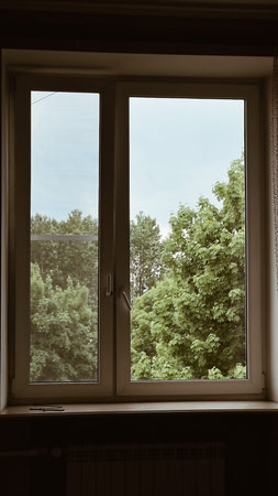 Atmospheric vintage style window in dark room with view on green trees. Summer view out of window....