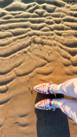 Vertical picture with top view of stylish cowboy leather shoes on textured sand on sunny beach in...
