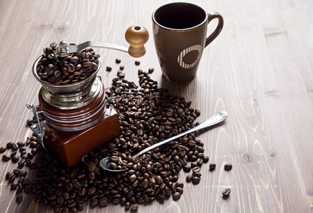 Coffee beans on brown wooden background. Coffee grinder and Cup with spoonの写真素材