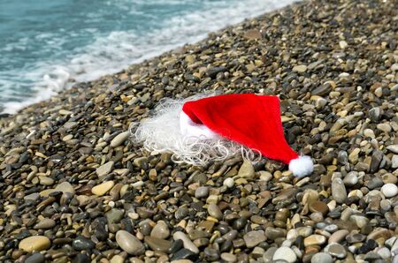 Santa Claus red hat and beard lie on sea shore on pebbles, Christmas concept and travelの写真素材