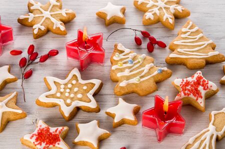 Beautiful homemade Christmas cookies with white icing, red candles and berries on wooden background, close-upの写真素材