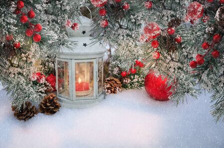 Beautiful Christmas lantern with candle and fir branches with cones and red berries in snow. Atmospheric winter scene with copy spaceの写真素材