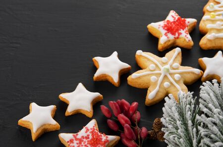 Christmas snow-covered spruce branch, home made star shaped cookies with icing on black background, copy spaceの写真素材
