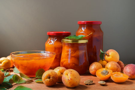 Apricot jam in a glass dish and jars. Fresh ripe apricots with leaves on the table. Homemade confiture.の写真素材