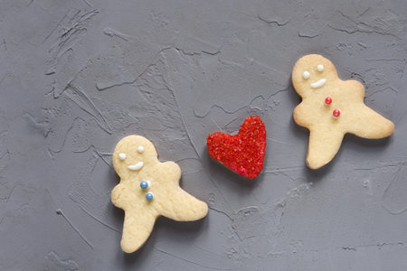 Love red heart between biscuit figures of a man and a woman on a grey background. Valentines day...