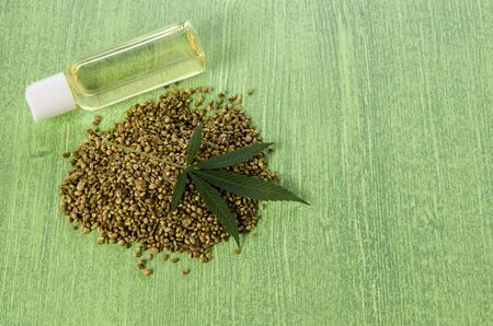 Hemp oil in a glass bottle, seeds with green leaves on a green wooden background, copy spaceの写真素材