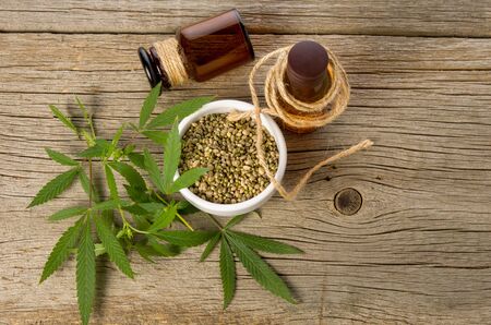 Hemp cosmetic or cooking oil in brown glass bottles, seeds and green cannabis leaves on wooden table background.の写真素材