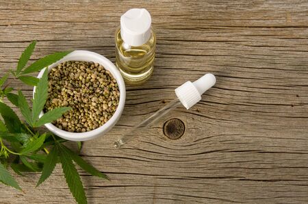 Hemp oil in glass bottle, seeds with green leaves and pipette on wooden rustic table backgroundの写真素材