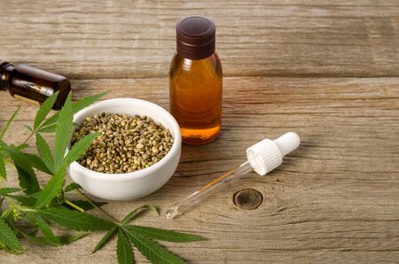 Hemp oil in glass bottle, seeds and leaves on wooden table background. Cosmetics or healthy diet concept.の写真素材