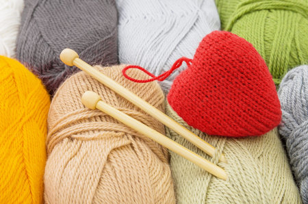 Color  yarn skeins, knitting needles and red heart, close up. The concept of knitting and...