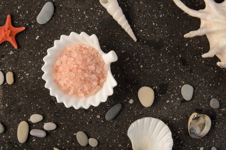 Pink sea salt for baths in a white porcelain plate on a dark stone background with shells close up