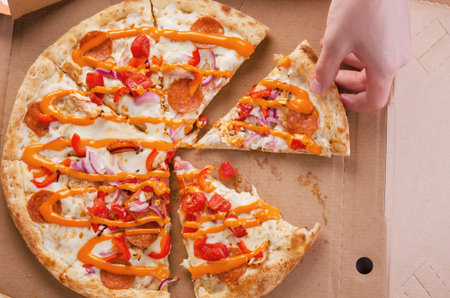Human hand picks up pizza fast food in cardboard box cut into pieces