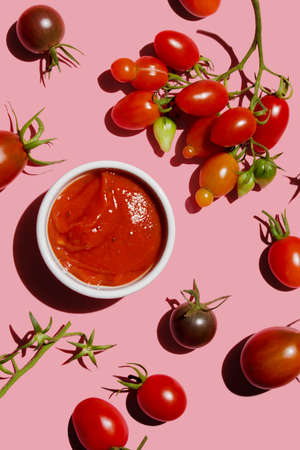 Tomato ketchup sauce and ripe red raw tomatoes on pink colored background, top viewの写真素材