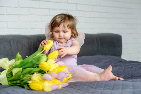 Cute little girl with tulips in fairy clothes sits on a bed. Spring mood