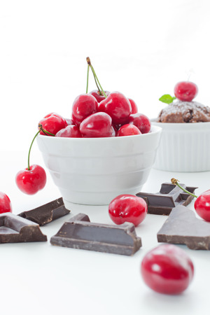 Cherries in white bowl with chocolate and cupcake on white backgroundの写真素材