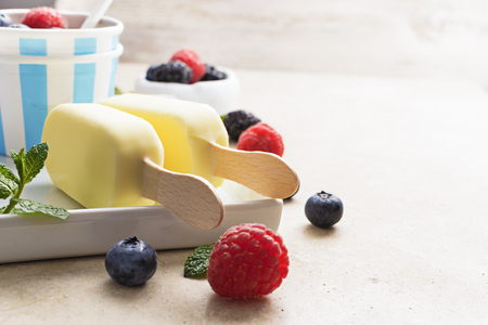 Vanilla ice cream popsicles coat with  white chocolate  with  fresh berries on wooden, marble   background. Summer food concept. Free text space, selective focus.の写真素材