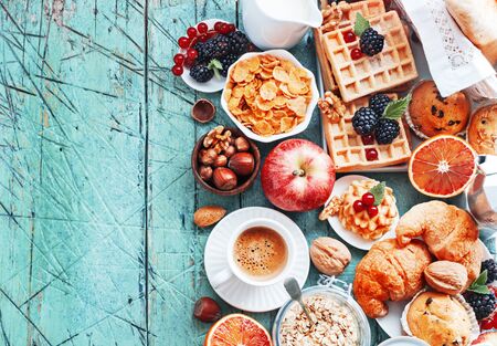 Healthy and colorful breakfast - cup of coffee with homemade granola, waffles, muffins,almond,hazelnuts,various fresh fruits, berries and milk on old wooden table.の写真素材