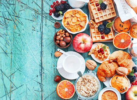 Healthy and colorful breakfast - cup of coffee with homemade granola, waffles, muffins,almond,hazelnuts,various fresh fruits, berries and milk on old wooden table.の写真素材