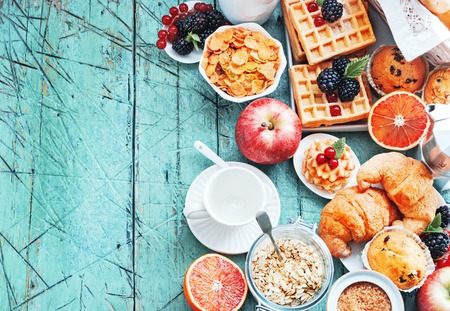 Healthy and colorful breakfast - cup of coffee with homemade granola, waffles, muffins,almond,hazelnuts,various fresh fruits, berries and milk on old wooden table.の写真素材