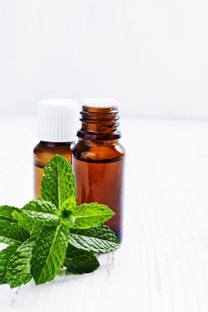 Essential oil of peppermint in dark bottles, fresh green mint on white wooden background, selective focusの写真素材