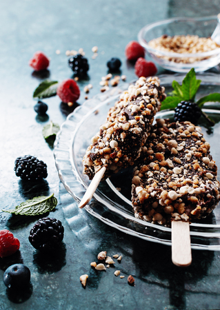 Peanut chocolate butter ice cream popsicles on dark marble table with fresh summer berries. Selective focus, top view, free text space.の写真素材