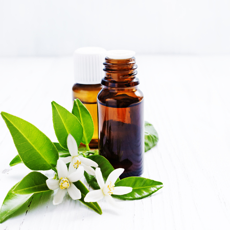 Neroli (Citrus aurantium) essential oil in a brown glass bottle with fresh white  flowers on ligth background. Selective focus.の写真素材