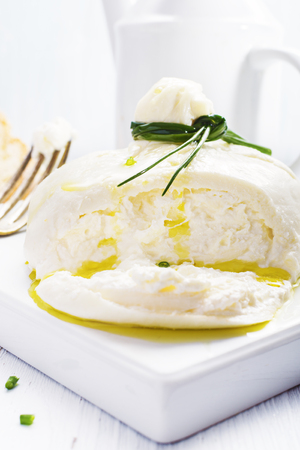 Italian burrata cheese with basil onion olive oil on white   plate on light background. Selective focus, free text space.の写真素材