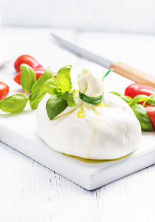 Italian burrata cheese with basil onion olive oil on white   plate on light background. Selective focus, free text space.の写真素材