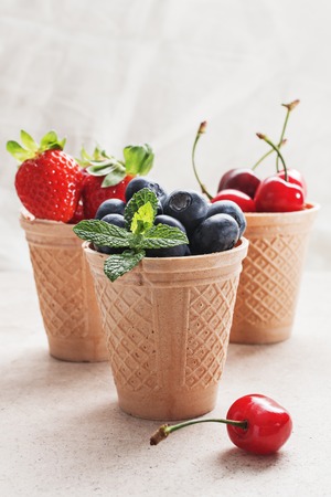 Waffle cones with fresh berries, ingredients for ice cream,sorbet or granita on marble surface.の写真素材
