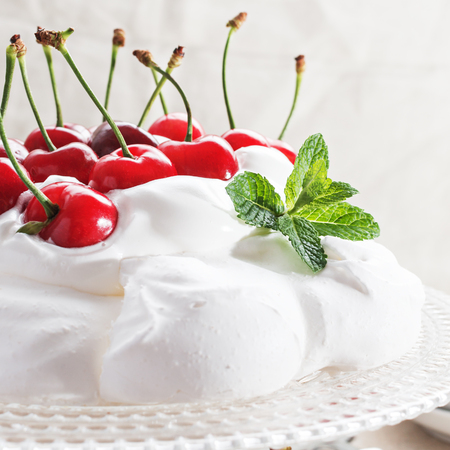 Pavlova - meringue cake with  fresh cherries  on  glass cake stand on marble background, copy space, close up, selective focus.の写真素材