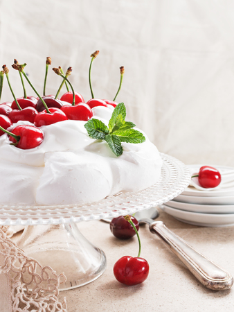 Pavlova - meringue cake with  fresh cherries  on  glass cake stand on marble background, copy space, close up, selective focus.の写真素材