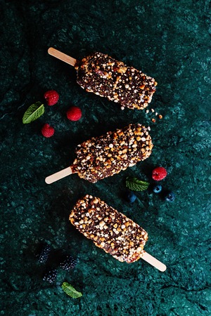 Peanut chocolate butter ice cream popsicles on dark marble table with fresh summer berries. Selective focus, top view, free text space.の写真素材