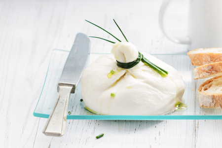 Burrata, fresh Italian cheese with bread on a wooden light background.