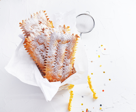 Italian Frappe or chiacchiere  - typical Italian carnival fritters dusted with powdered sugar on  white wooden table. With free text space.の写真素材