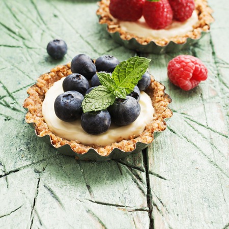 Mini oat flakes tart with cream and blueberries and mint on white wooden table with free text spaceの写真素材