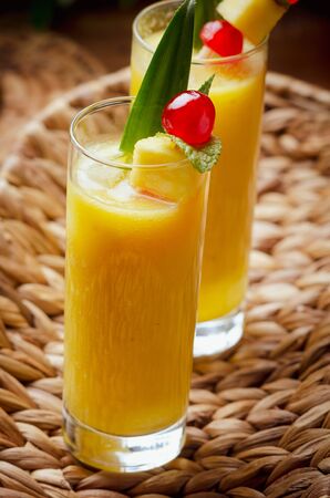 Tropical  cocktail pineapple  in a glasses, garnished with  cherries maraschino on wooden  table .の写真素材