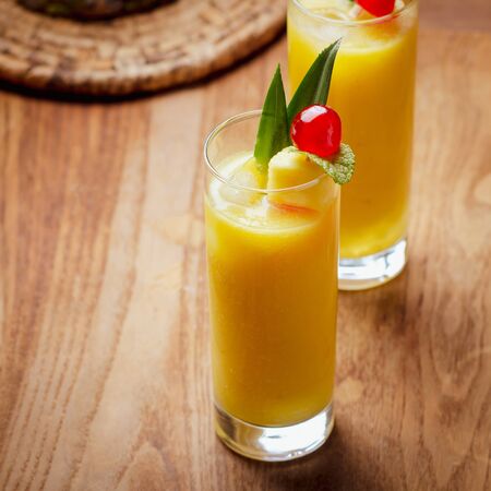 Tropical  cocktail pineapple  in a glasses, garnished with  cherries maraschino on wooden  table .の写真素材