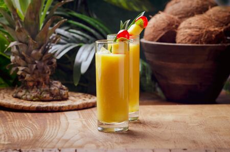 Tropical  cocktail pineapple  in a glasses, garnished with  cherries maraschino on wooden  table .の写真素材