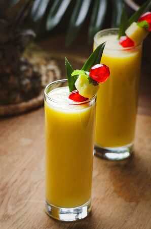 Tropical  cocktail pineapple  in a glasses, garnished with  cherries maraschino on wooden  table .の写真素材