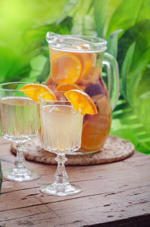 Glass jug of white sparkling wine sangria decorated with citrus slices and season fruits on wooden table.の写真素材
