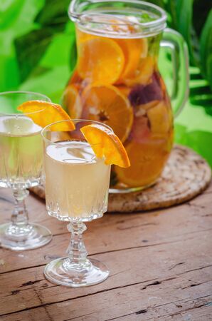 Glass jug of white sparkling wine sangria decorated with citrus slices and season fruits on wooden table.の写真素材
