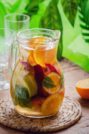Glass jug of white sparkling wine sangria decorated with citrus slices and season fruits on wooden table.の写真素材