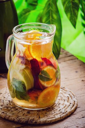 Glass jug of white sparkling wine sangria decorated with citrus slices  and season fruits on wooden table.の写真素材