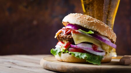 Traditional burgers with cutlet, fresh vegetables, crispy bun with sesame seeds with glass beer on a wooden  table.の写真素材
