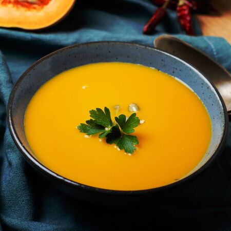 Pumpkin soup in blue bowl with pasrley and seeds.の写真素材