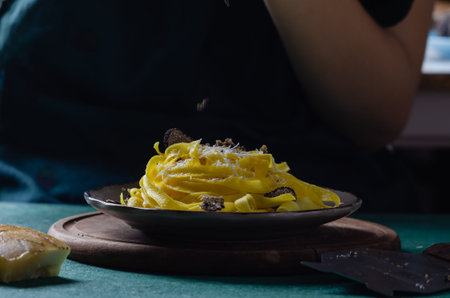 Female hands grating parmesan cheese, black truffle onto pasta tagliatelle.の写真素材