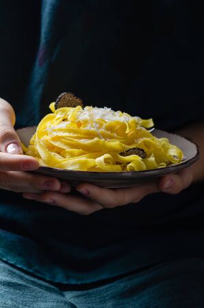 Female hands holding plate with pasta tagliatelle with parmesan cheese and black truffle.の写真素材
