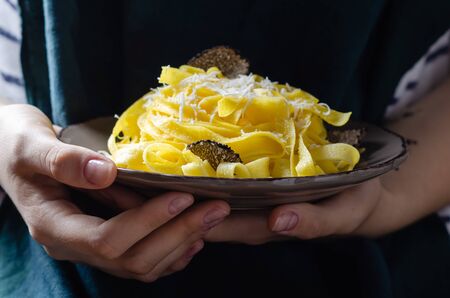 Female hands holding plate with pasta tagliatelle with parmesan cheese and black truffle.の写真素材