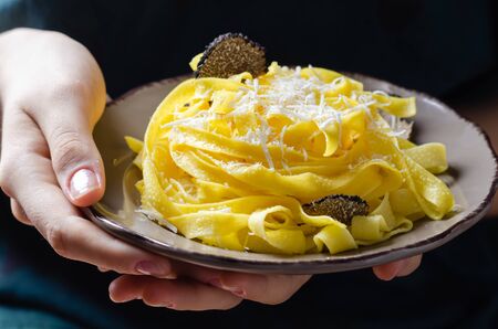 Female hands holding plate with pasta tagliatelle with parmesan cheese and black truffle.の写真素材