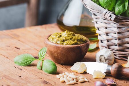 Pesto sauce in a olive wooden bowl with pine nuts, basil, parmesan and garlic over rustic table.の写真素材
